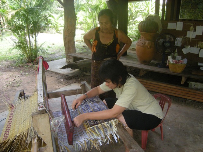woman at a weaving loom with another woman standing beside
