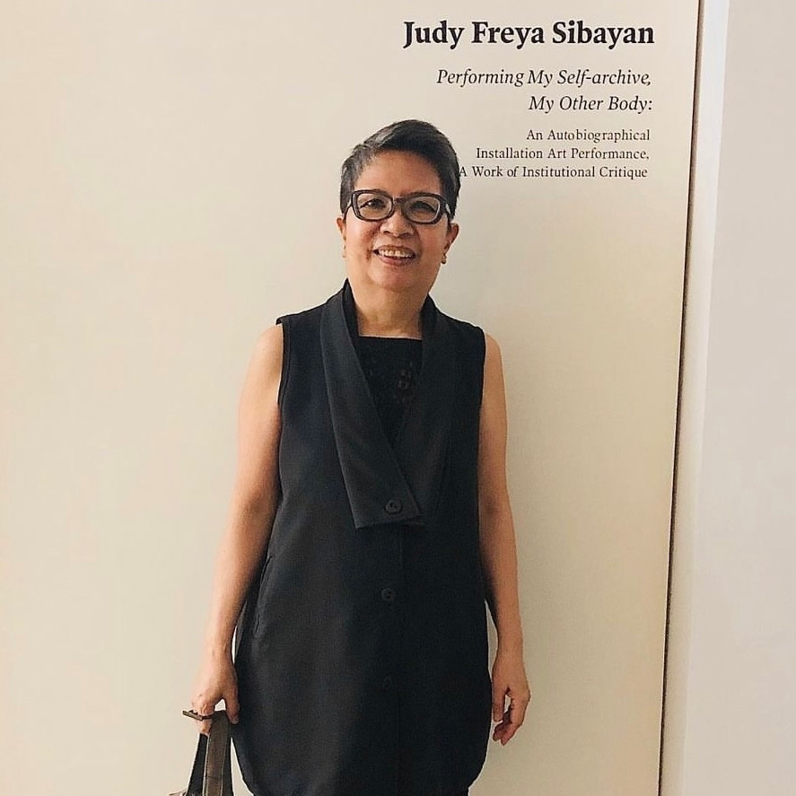 woman with short grey hair wearing a black dress with cowl neck